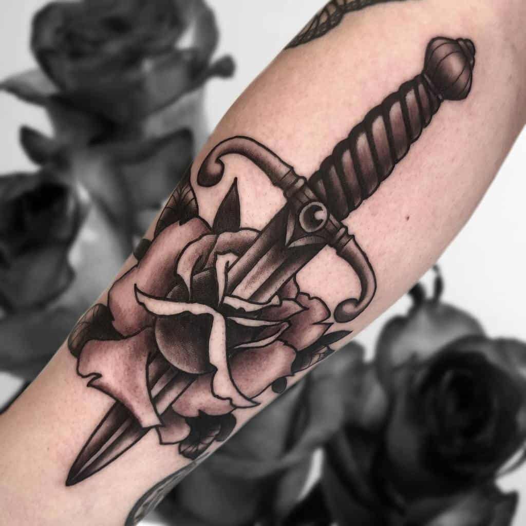 A tattoo of a dagger through a rose on a forearm