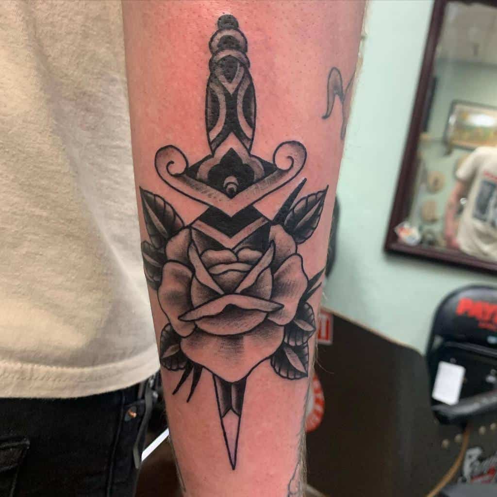 Black and grey tattoo of a dagger piercing a rose on a forearm