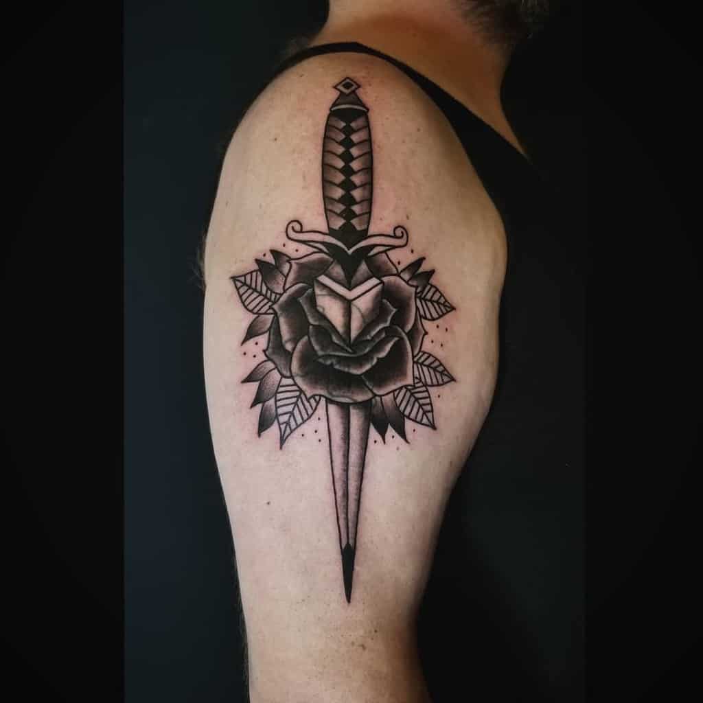 A dagger pierced through a rose tattoo on a man's upper arm