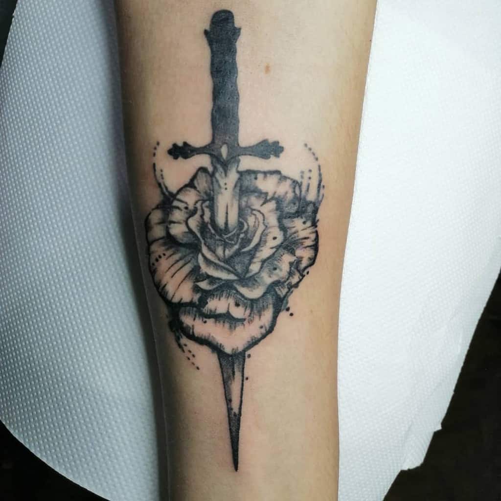 Traditional tattoo of a sword piercing a rose on a forearm
