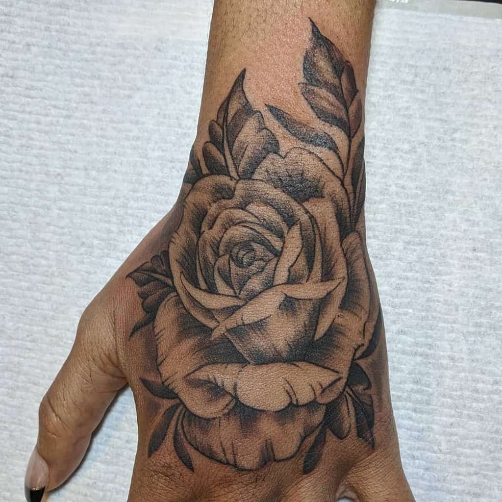 A hand adorned with an exquisitely detailed rose tattoo gracing the back