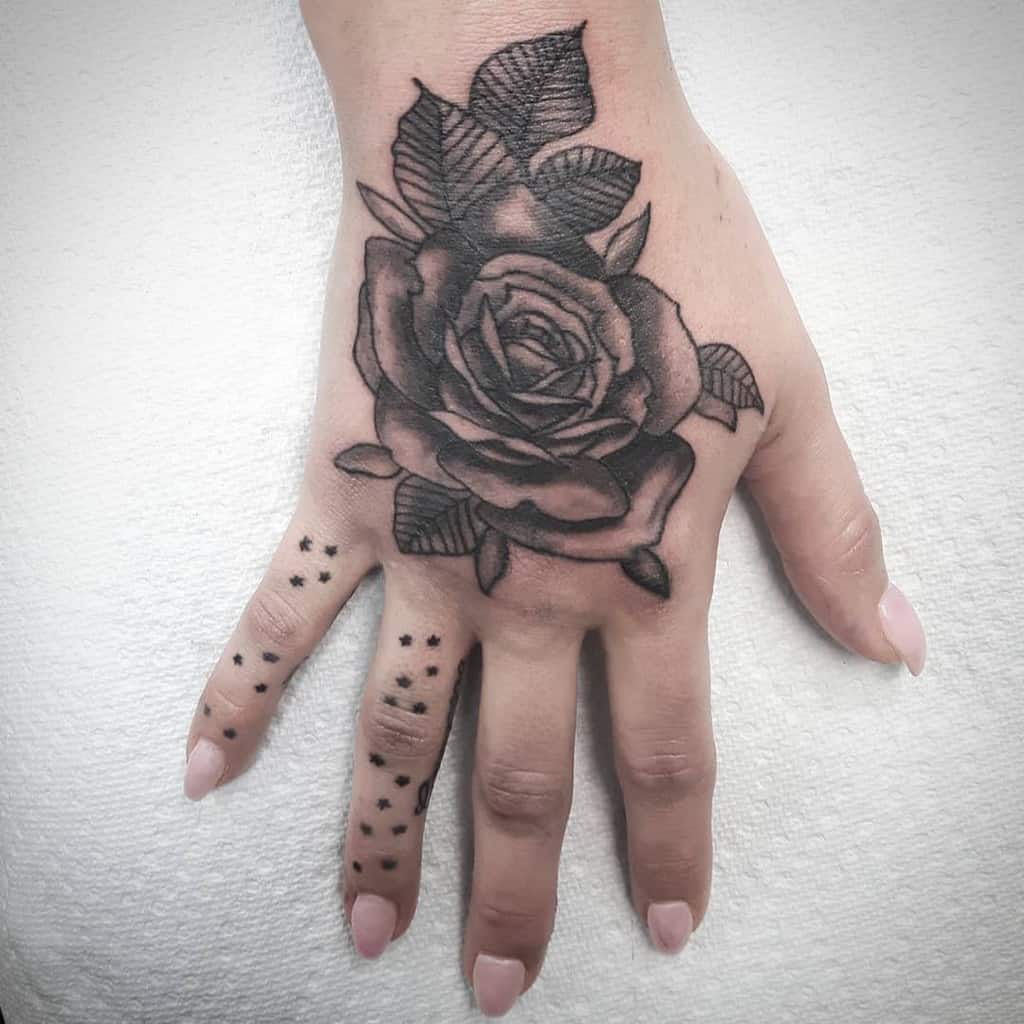 A hand adorned with a delicate rose tattoo and accented by small dots on the fingers
