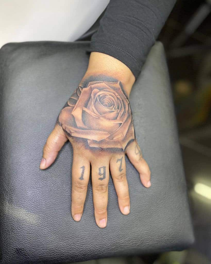 A captivating hand tattoo featuring a large, intricate rose covering the back and the bold numbers "1974" elegantly etched on the fingers