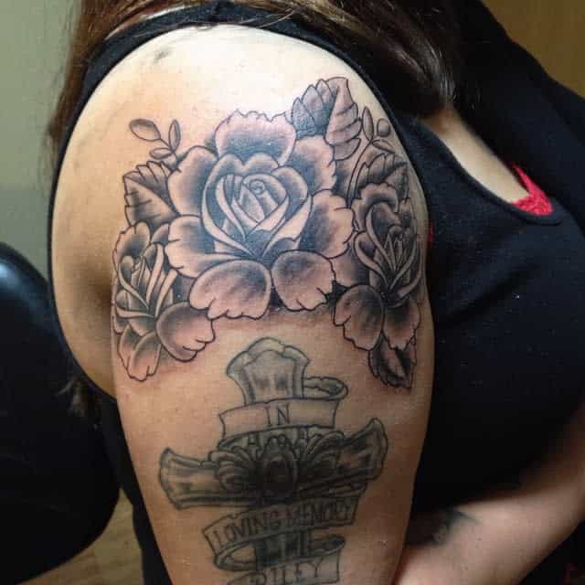 Tattoo of large roses and a cross with text elegantly wrapping around the shoulder