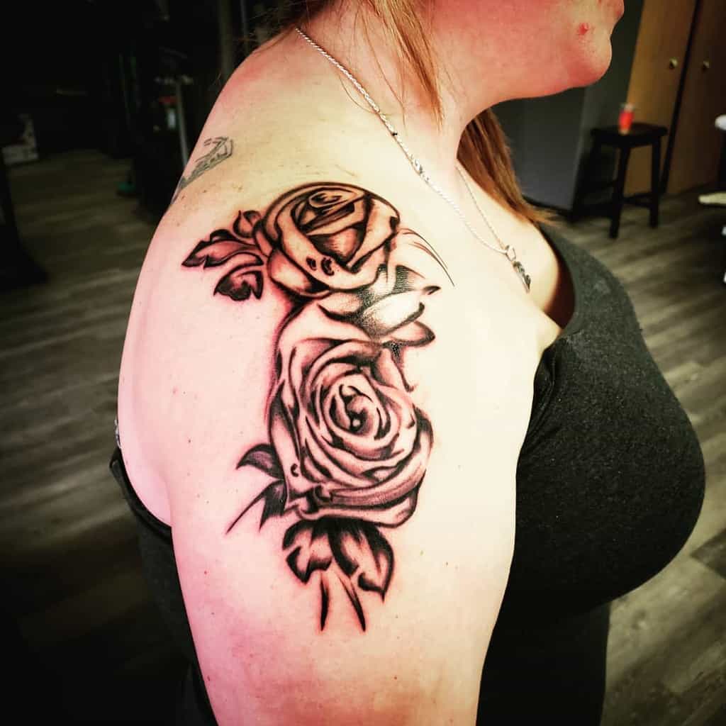 A woman with a detailed black rose tattoo beautifully intertwines over her shoulder and upper arm