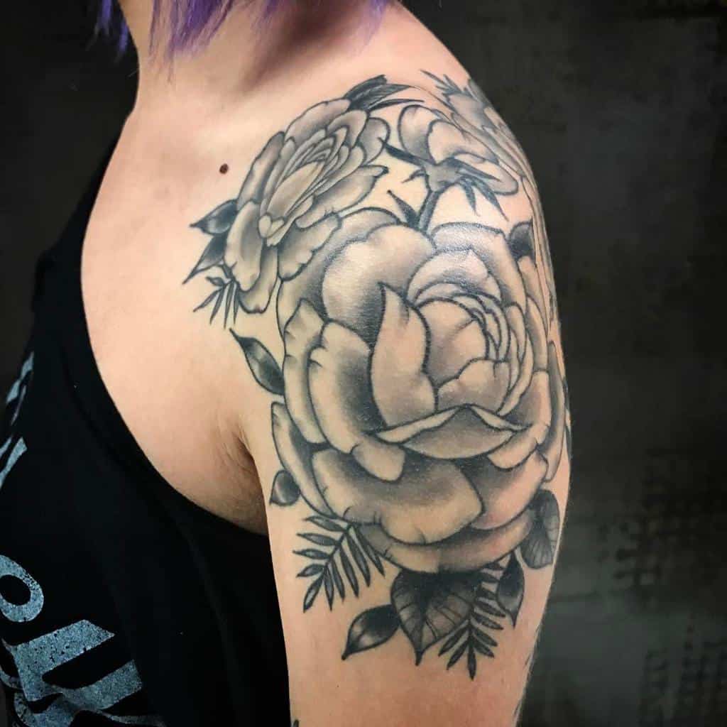 A stunning black and gray floral tattoo cascades beautifully across the woman's shoulder and upper arm, capturing a delicate balance of artistry and elegance