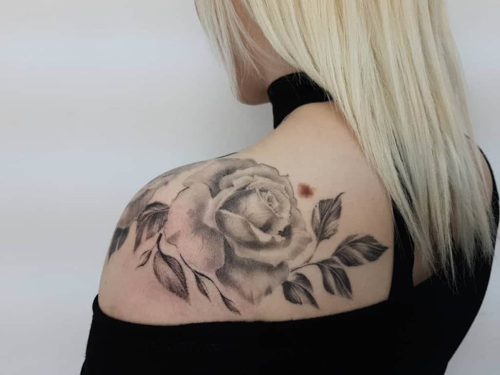 A detailed black and grey rose tattoo on the shoulder, showcasing a single rose with soft shading and delicate leaves