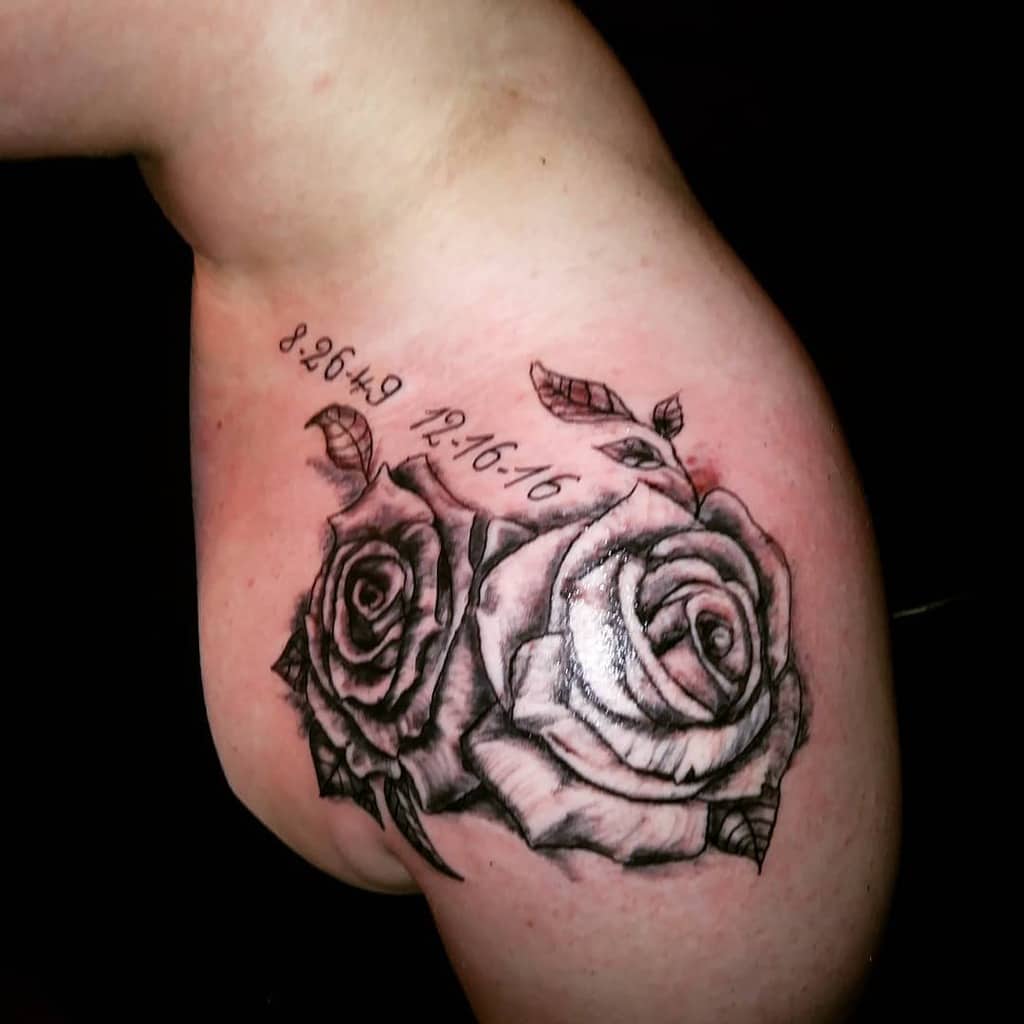 A pair of elegantly shaded roses graces the shoulder, with significant dates etched above them