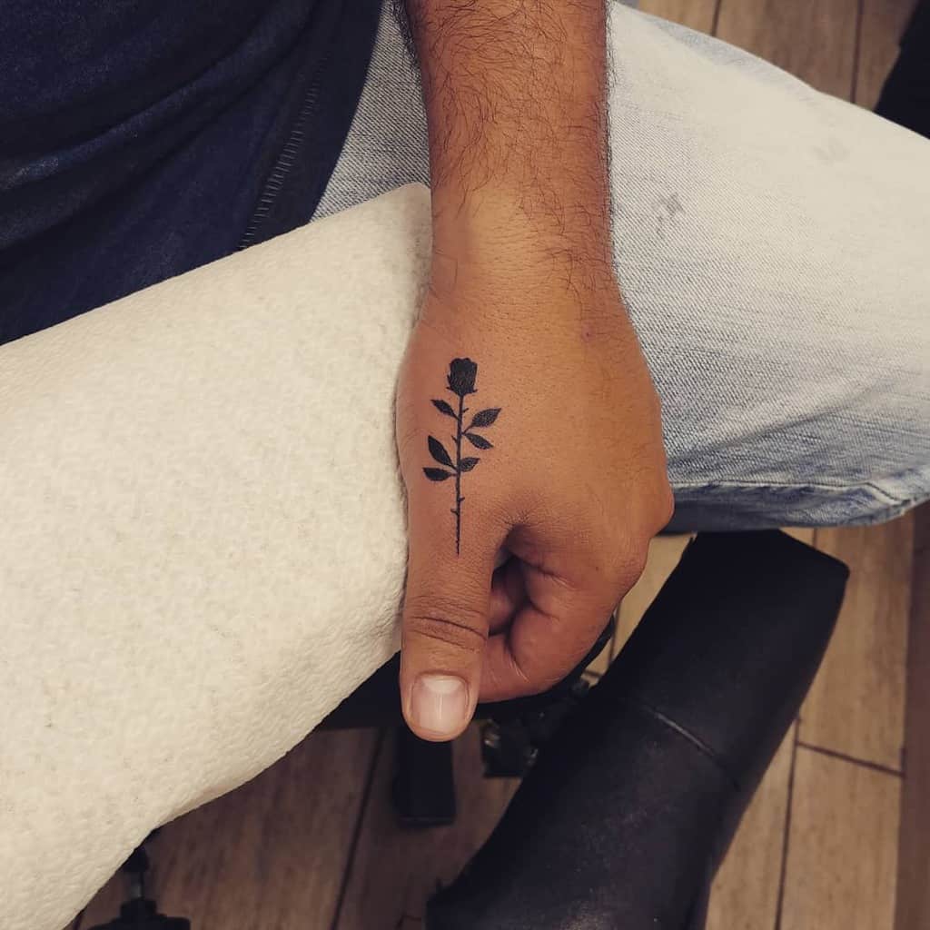 Tattoo of a black rose on a person's hand, near the thumb