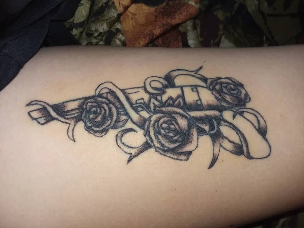 Blackwork tattoo featuring a revolver intertwined with blooming roses and flowing vines, blending elegance with bold design