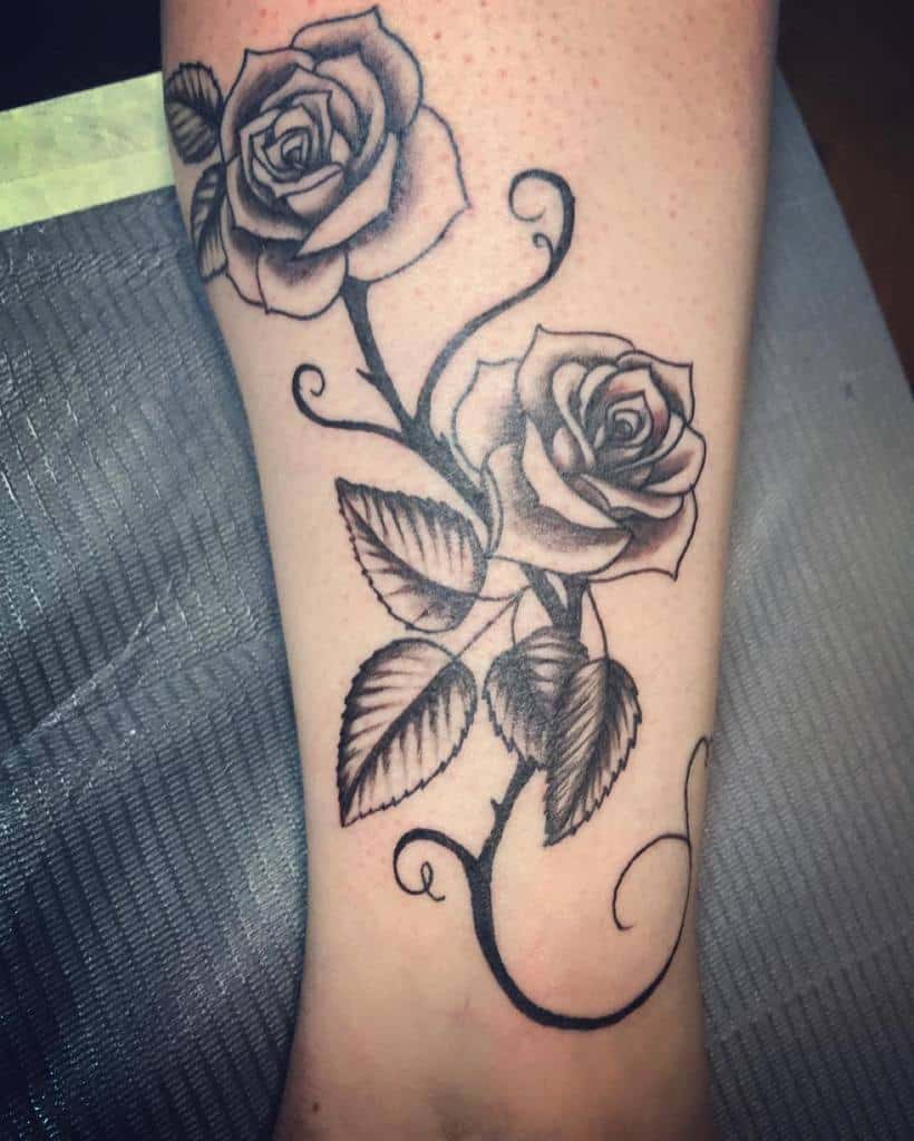 Blackwork tattoo featuring two beautifully shaded roses with flowing stems and leaves, elegantly curving along the forearm