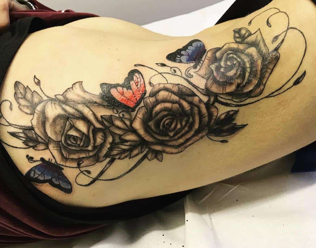 Elegant tattoo featuring a cluster of detailed roses with swirling vines, accented by vibrant red and blue butterflies for a striking contrast