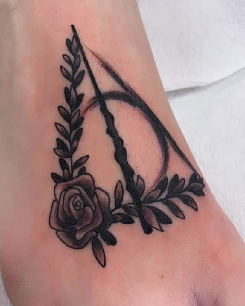 Minimalist tattoo featuring a rose intertwined with leafy branches, forming a geometric triangular design with bold blackwork accents