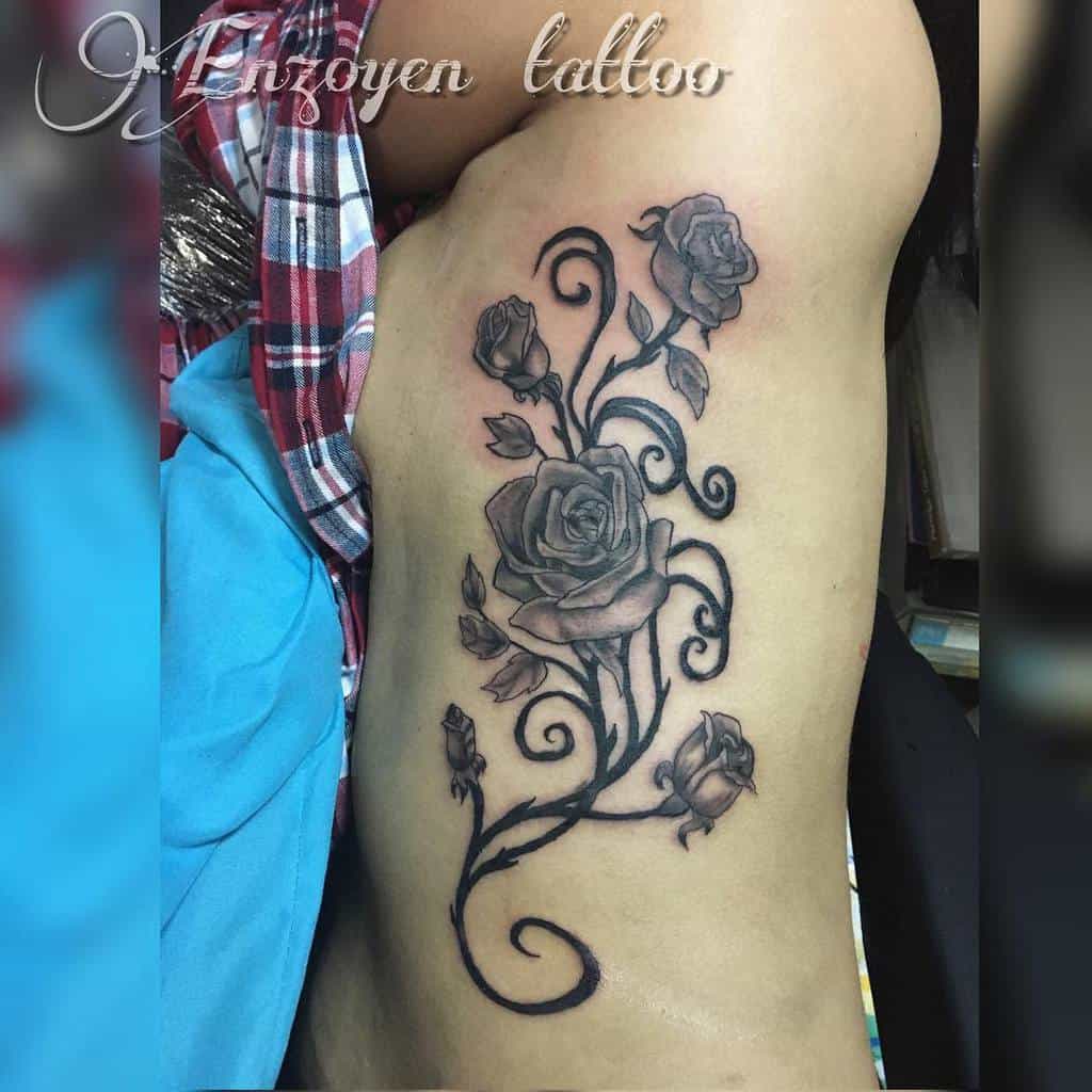 Graceful rib tattoo showcasing a vertical arrangement of intricately shaded roses connected by flowing vines and delicate leaves
