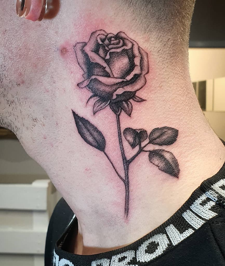 A neck tattoo featuring a detailed black and gray rose with elegantly flowing leaves and a slender stem