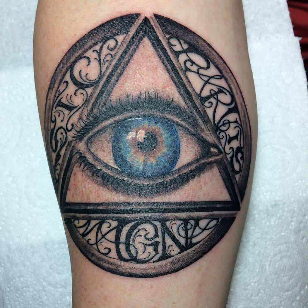 Tattoo of a blue eye inside a triangle, surrounded by ornate swirls and patterns