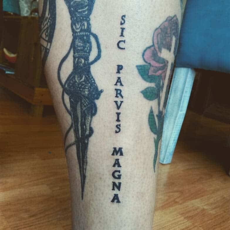 Leg tattoo featuring a dagger and the text "Sic Parvis Magna" with floral designs alongside