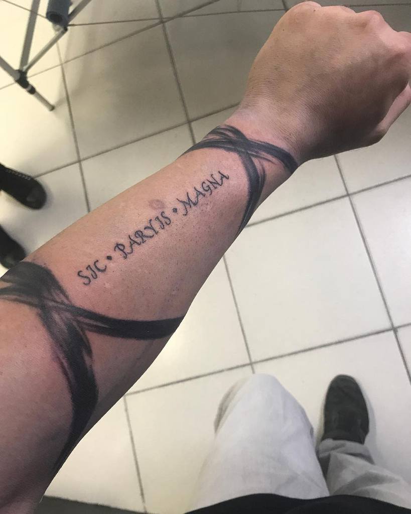 Forearm tattoo with "Sic Parvis Magna" surrounded by black abstract design