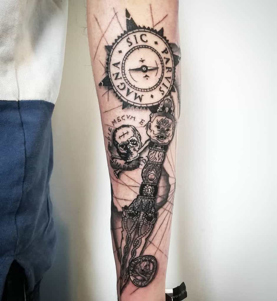 Forearm tattoo with a compass reading 'Sic Parvis Magna,' skulls, and intricate dagger details in a blackwork design style