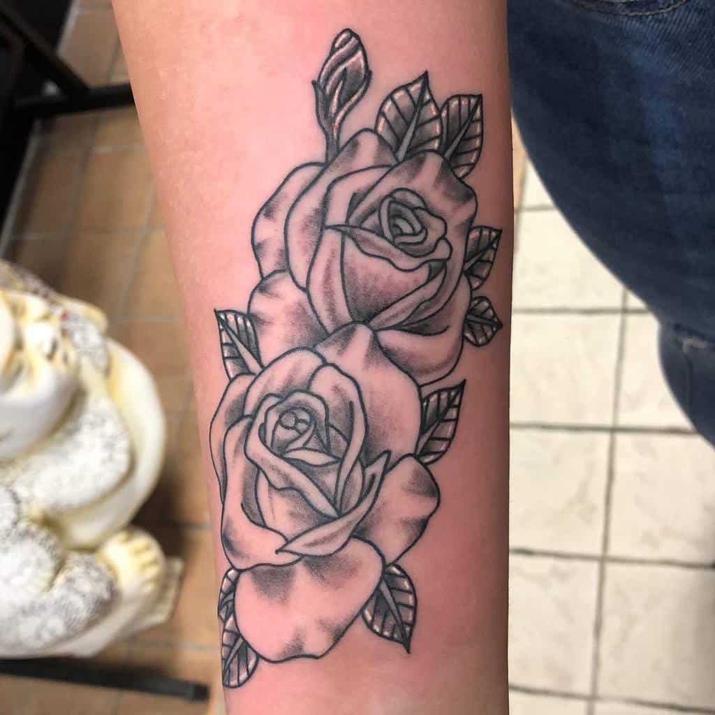 Black and white rose tattoo on forearm with detailed leaves