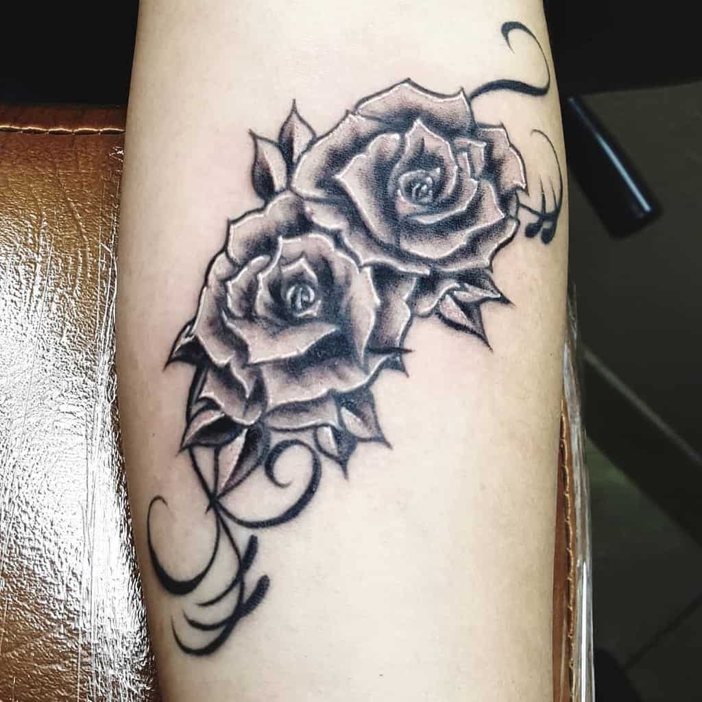 Tattoo of two shaded roses with swirling vines on forearm