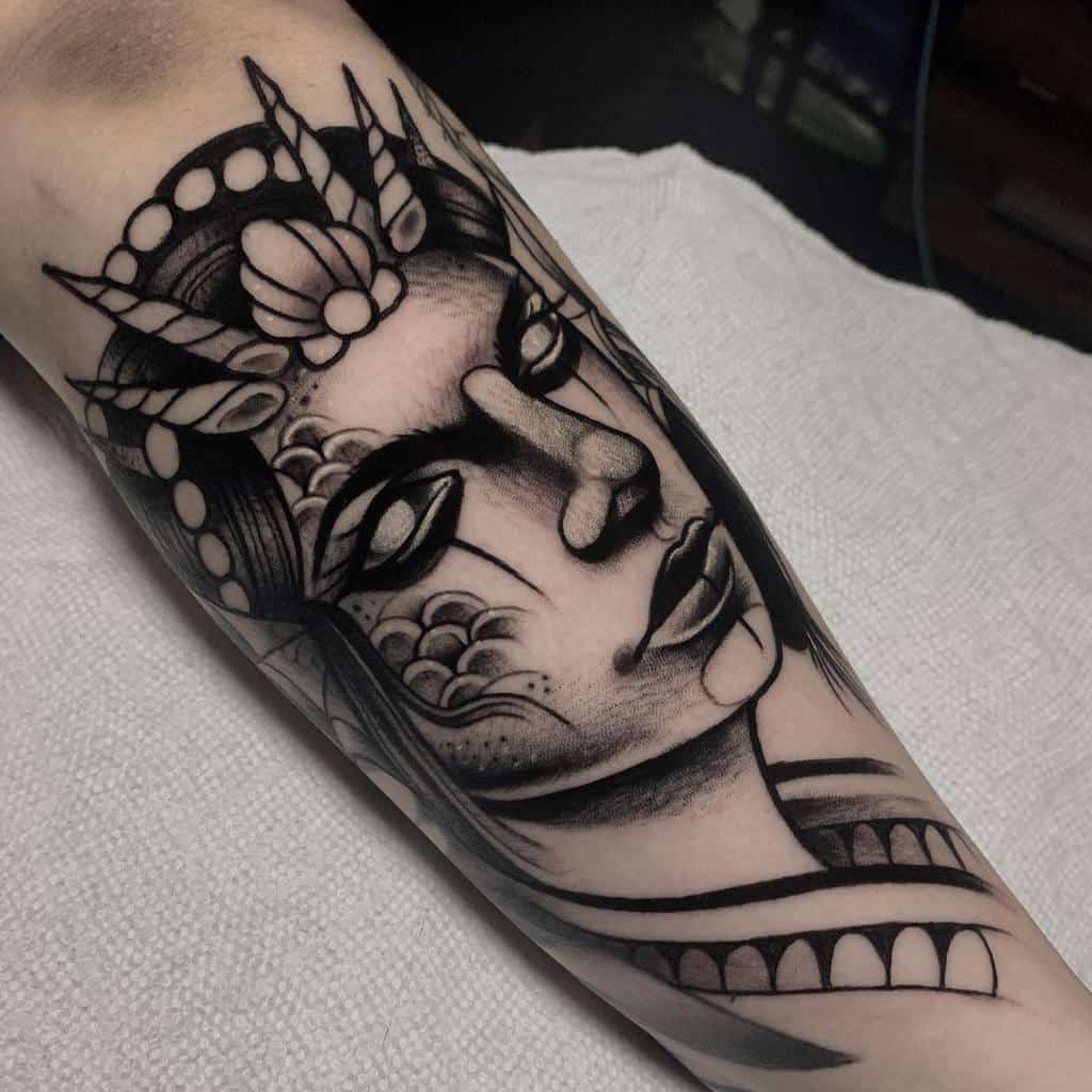 Black and gray tattoo of a siren's abstract face with a crown and patterns on an arm