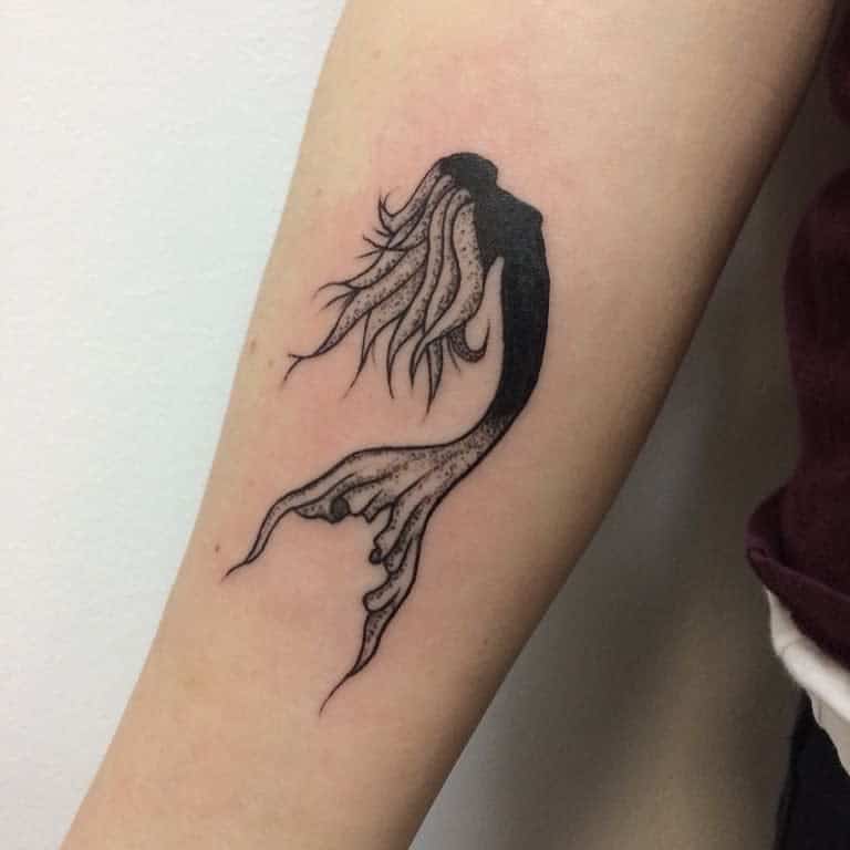 Minimalist blackwork tattoo of a mermaid's silhouette with flowing hair and detailed tail on the forearm