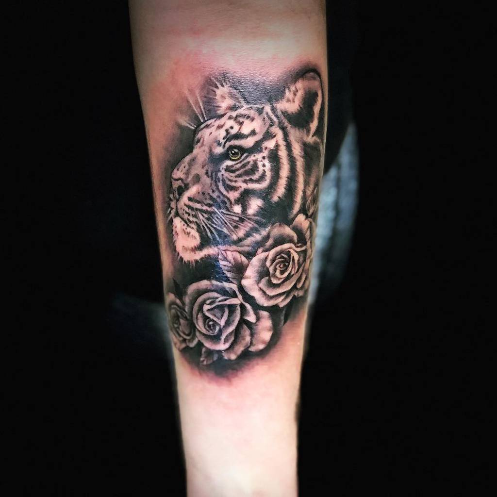 A majestic tiger intertwined with elegant roses, expertly inked in black and gray, graces the forearm