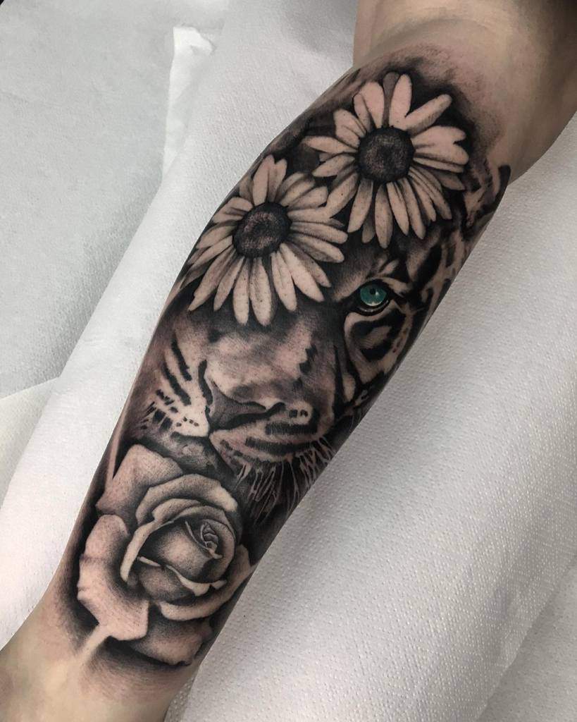 A striking tiger tattoo features daisies adorning its forehead and a graceful rose beneath, capturing the majestic blend of strength and nature