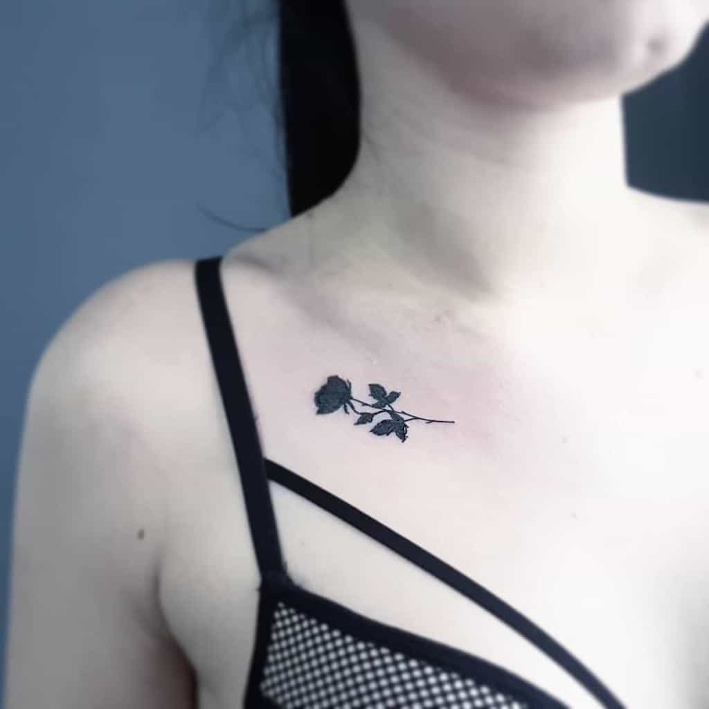 A tattoo of a delicate black rose is inked on a woman's upper chest