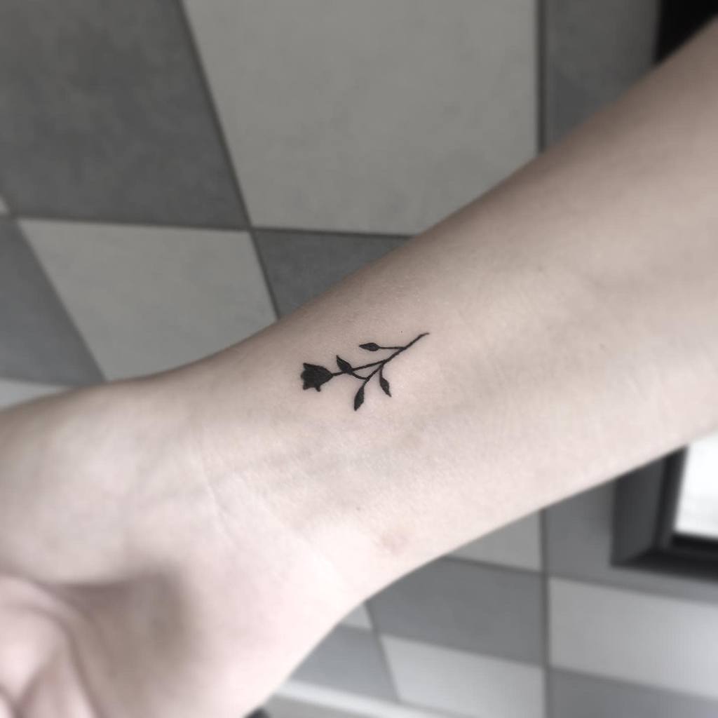 Small black floral tattoo on a forearm