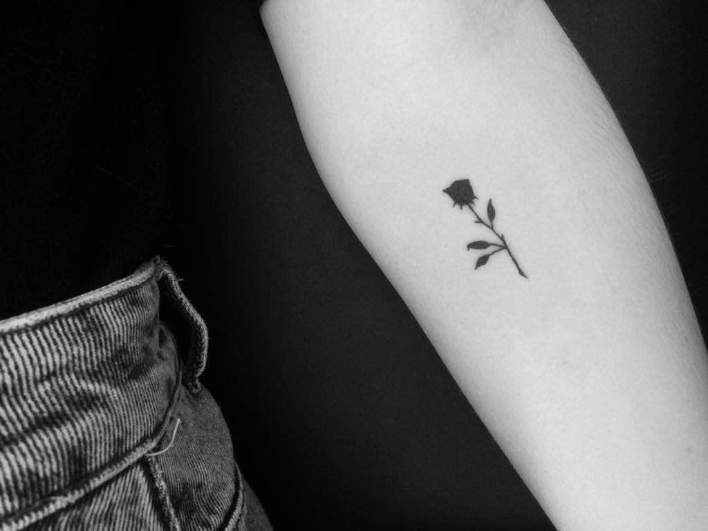 Black and white image of a small rose tattoo on a forearm