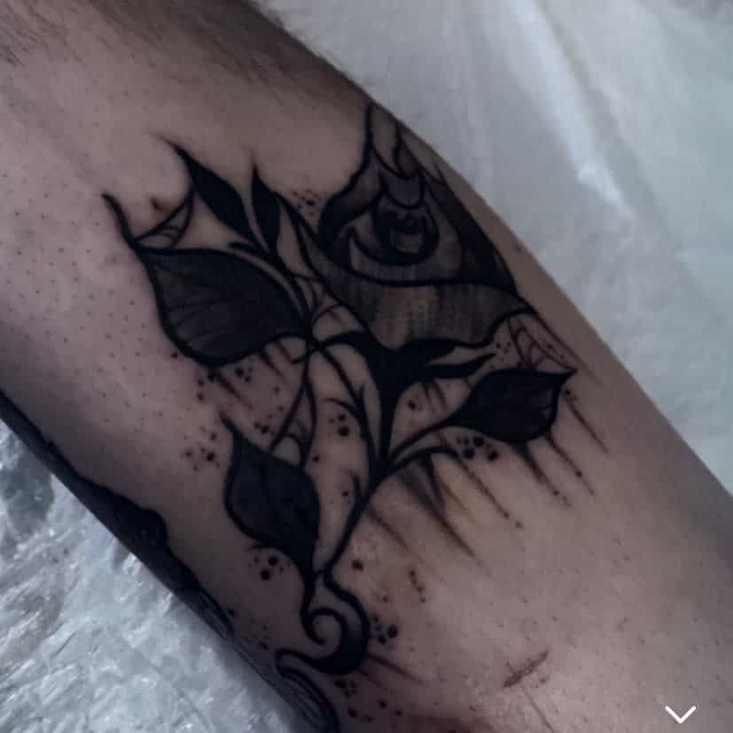 Black ink tattoo featuring a tribal floral design with leaves and an abstract rose seamlessly woven into the skin