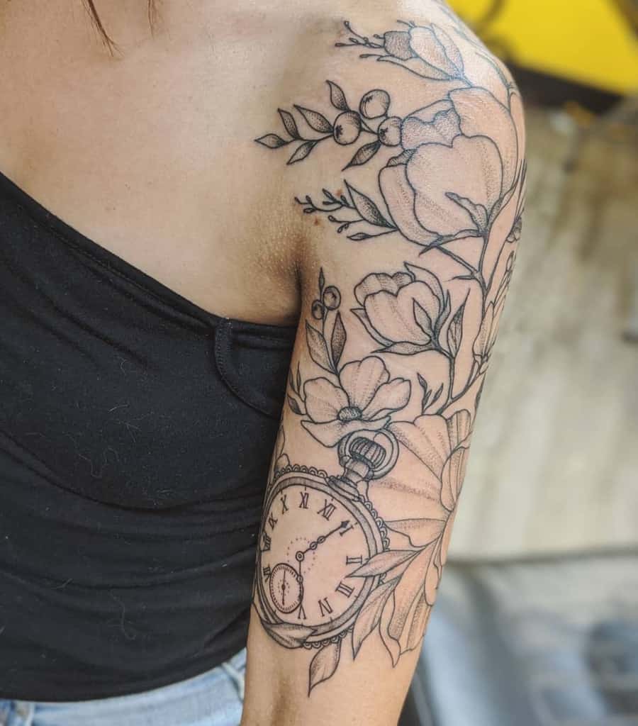 Upper arm tattoo of flowers and a pocket watch, in black ink design