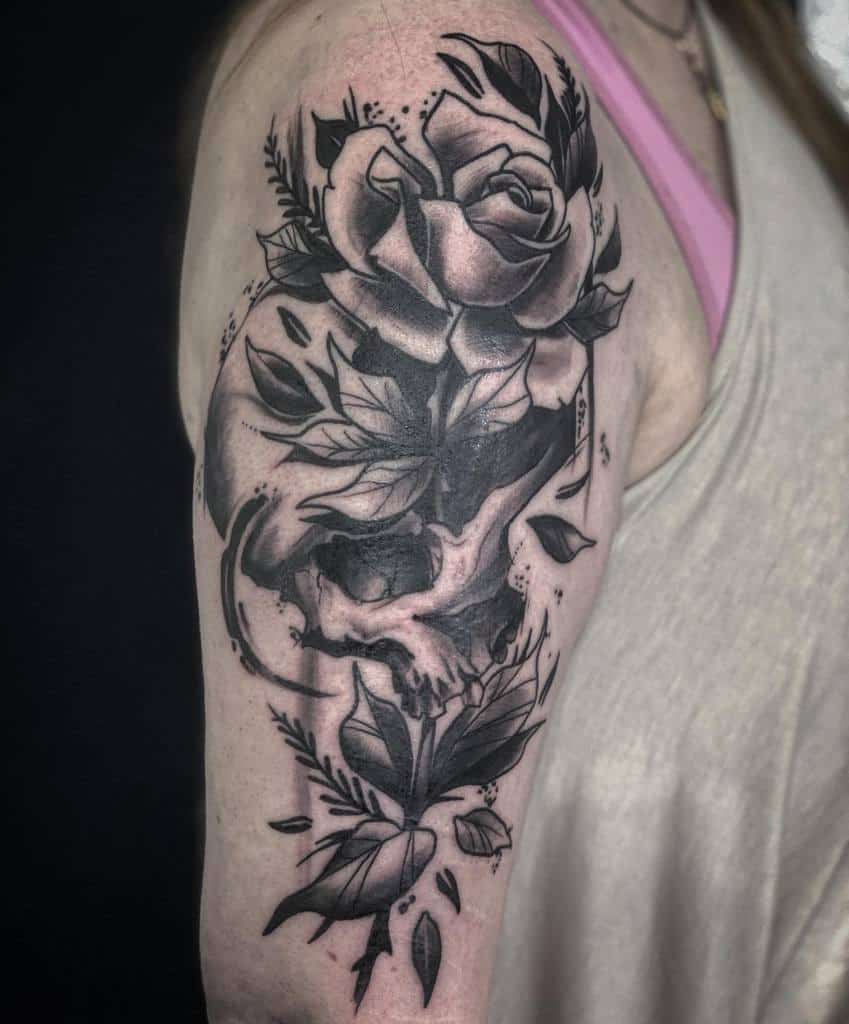 Black and grey tattoo of a rose and skull wrapped in leaves on a woman's upper arm
