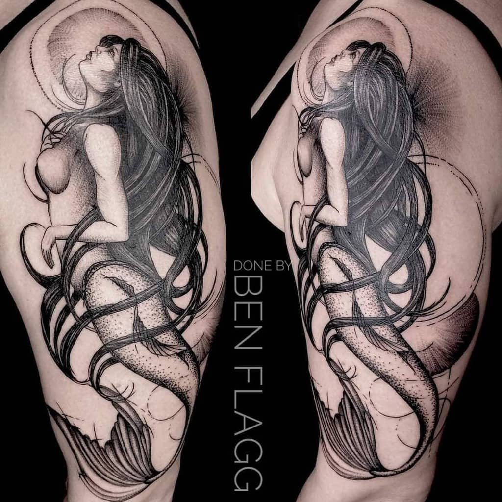 Detailed black ink tattoo of a mermaid with long hair on a woman's upper arm