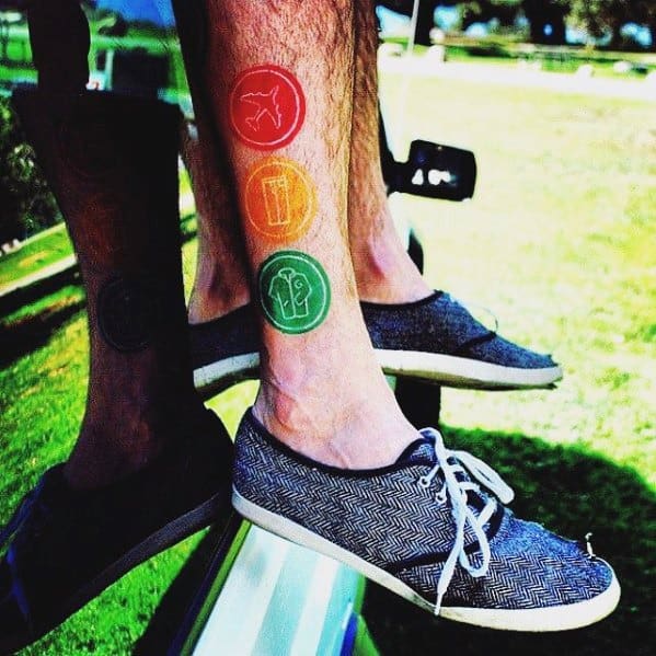 Tattoo featuring three colorful symbols inspired by Blink-182, arranged vertically on the leg, each in bold red, orange, and green hues.
