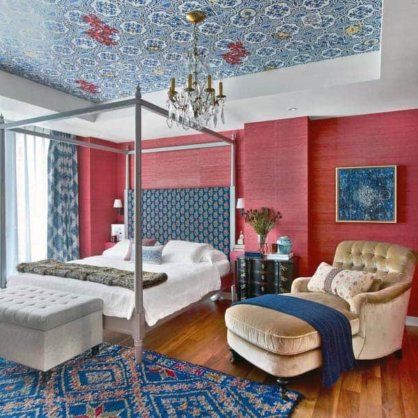 Vibrant bedroom with red walls, patterned ceiling, a red canopy bed, blue accents, and a cozy chaise lounge