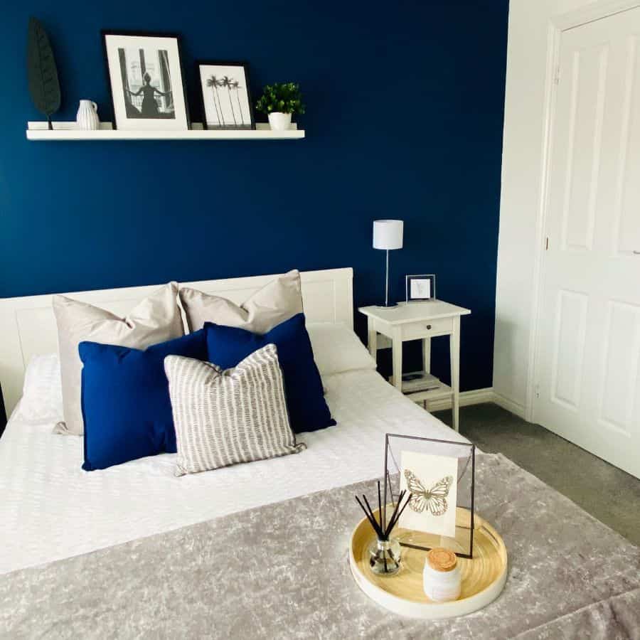 Stylish bedroom with navy blue accent wall, white bed, and decorative pillows.