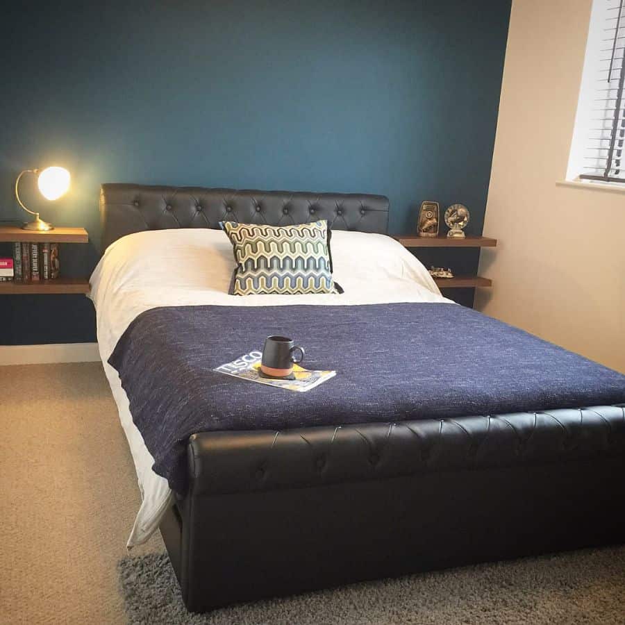 Modern bedroom with navy blue accent wall, leather bed frame, and cozy decor.