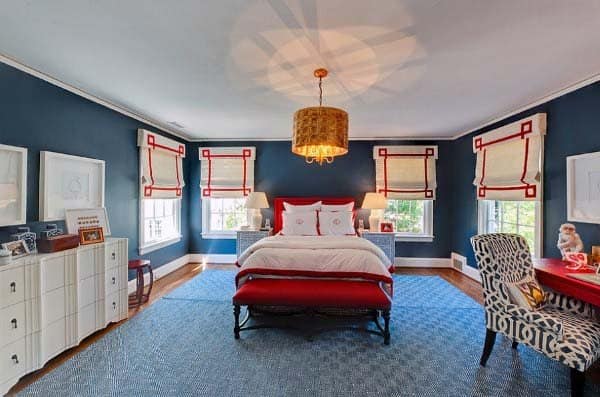 Bedroom with blue walls, red and white bedding, matching Roman shades, and patterned chairs.
