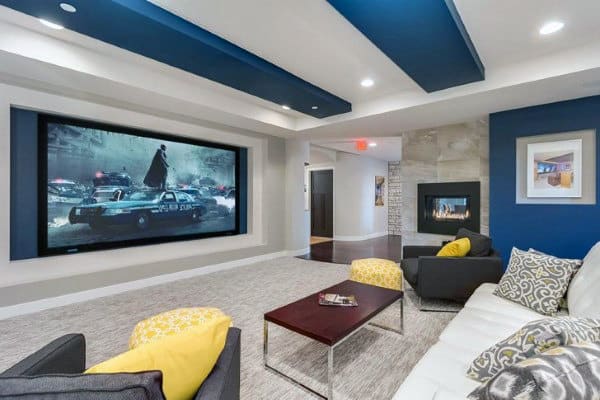 Modern home theater with large screen, cozy couches, yellow pillows, and recessed ceiling lights