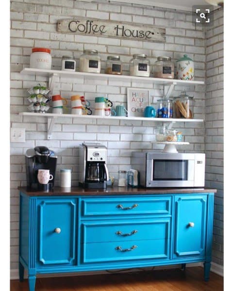 Coffee bar with blue cabinet, white brick wall, shelves, coffee machines, and a microwave.