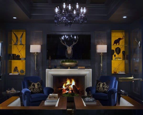 Elegant dark man cave with a lit fireplace, blue velvet chairs, and a chandelier