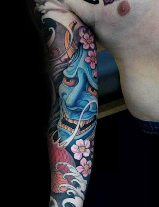 Full sleeve tattoo featuring a fierce blue Hannya mask, pink cherry blossoms, Japanese waves, and intricate shading for a bold design