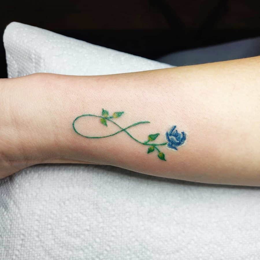 A delicate infinity tattoo with a blue rose and green leaves, symbolizing eternal growth and beauty.
