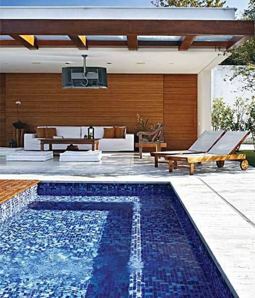 Modern pool with deep blue mosaic tiles, wooden patio lounge, and stylish outdoor seating area.