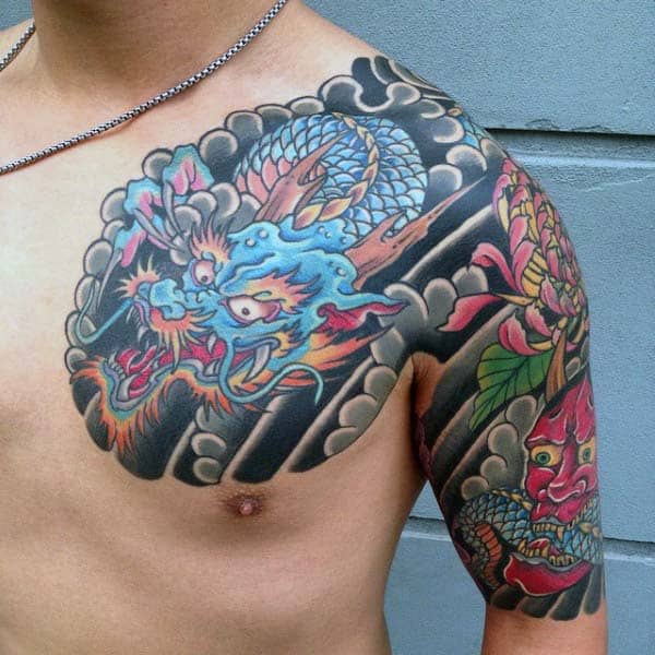 Dynamic Japanese tattoo design on the chest and upper arm, showcasing a vibrant blue dragon surrounded by bold clouds and colorful floral elements, creating a visually striking and symbolic piece