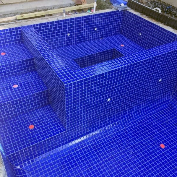 Vibrant blue mosaic tiles covering a modern pool with built-in seating and geometric design.
