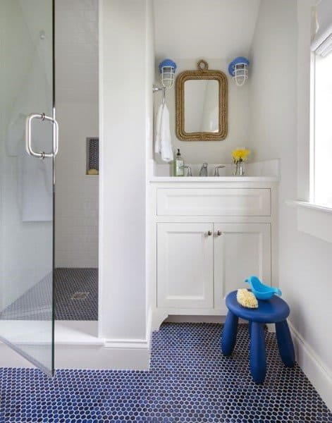 Small children's bathroom with blue hexagonal tile floor and glass shower enclosure.